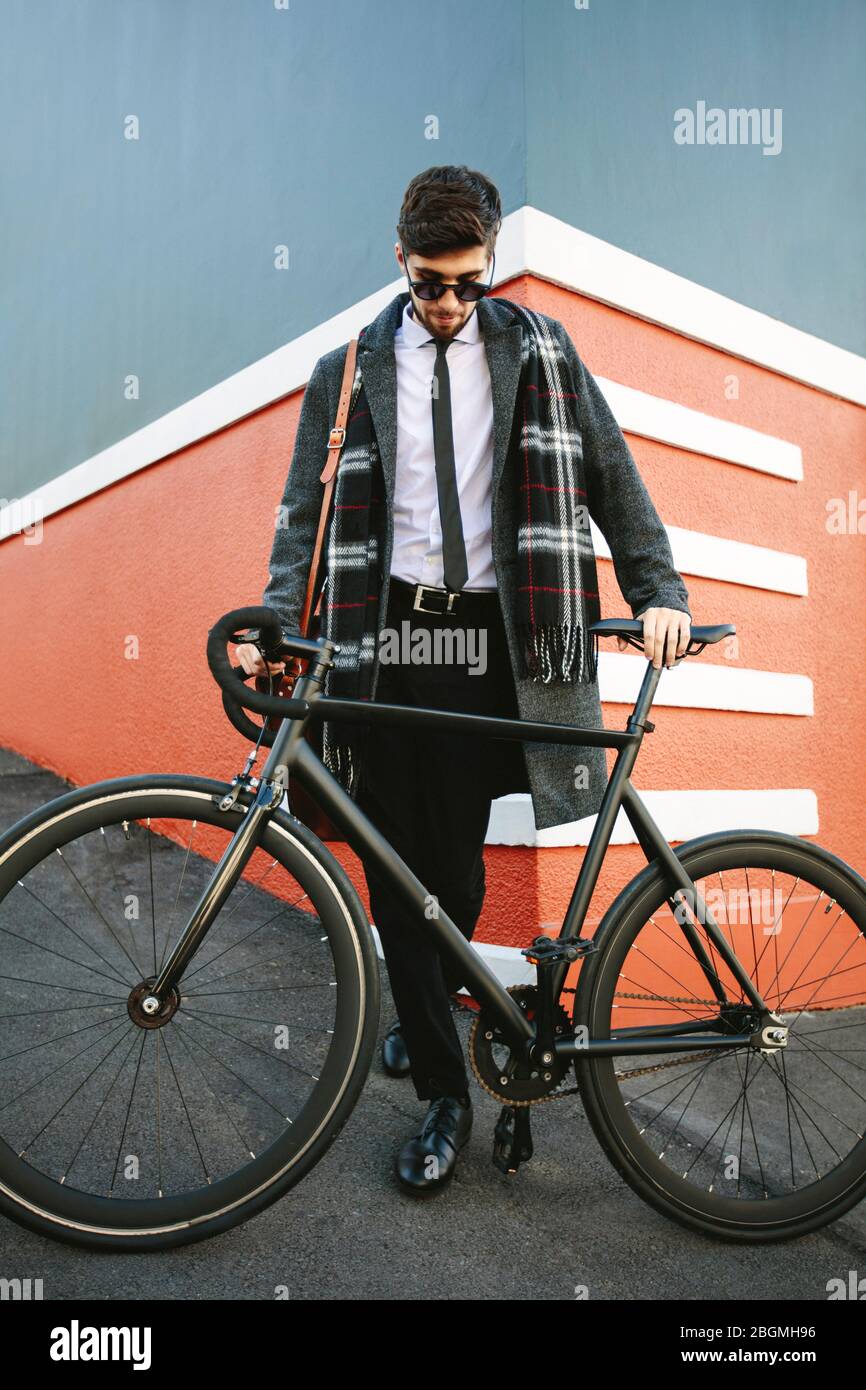 Un uomo d'affari alla moda che va a lavorare in bicicletta. Uomo in piedi accanto alla sua bicicletta su strada. Foto Stock