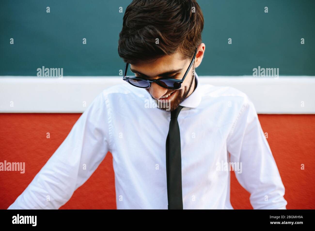 Uomo sorridente in abbigliamento formale e occhiali da sole in piedi all'aperto. uomo d'affari con cravatta bianca e nera che sorride all'aperto. Foto Stock