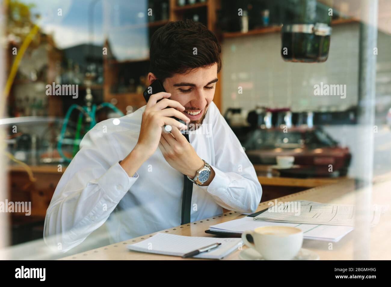 uomo d'affari che parla al telefono mentre lavora da un bar. Uomo che fa il suo lavoro seduto in un bar. Foto Stock