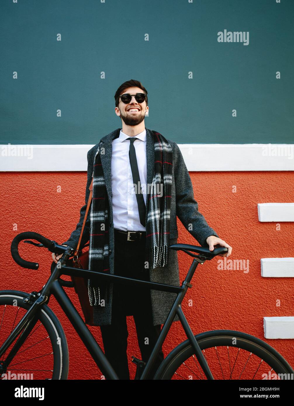 Uomo sorridente che andrà a lavorare in bicicletta. Uomo d'affari in piedi accanto alla sua moto sul marciapiede all'aperto. Foto Stock
