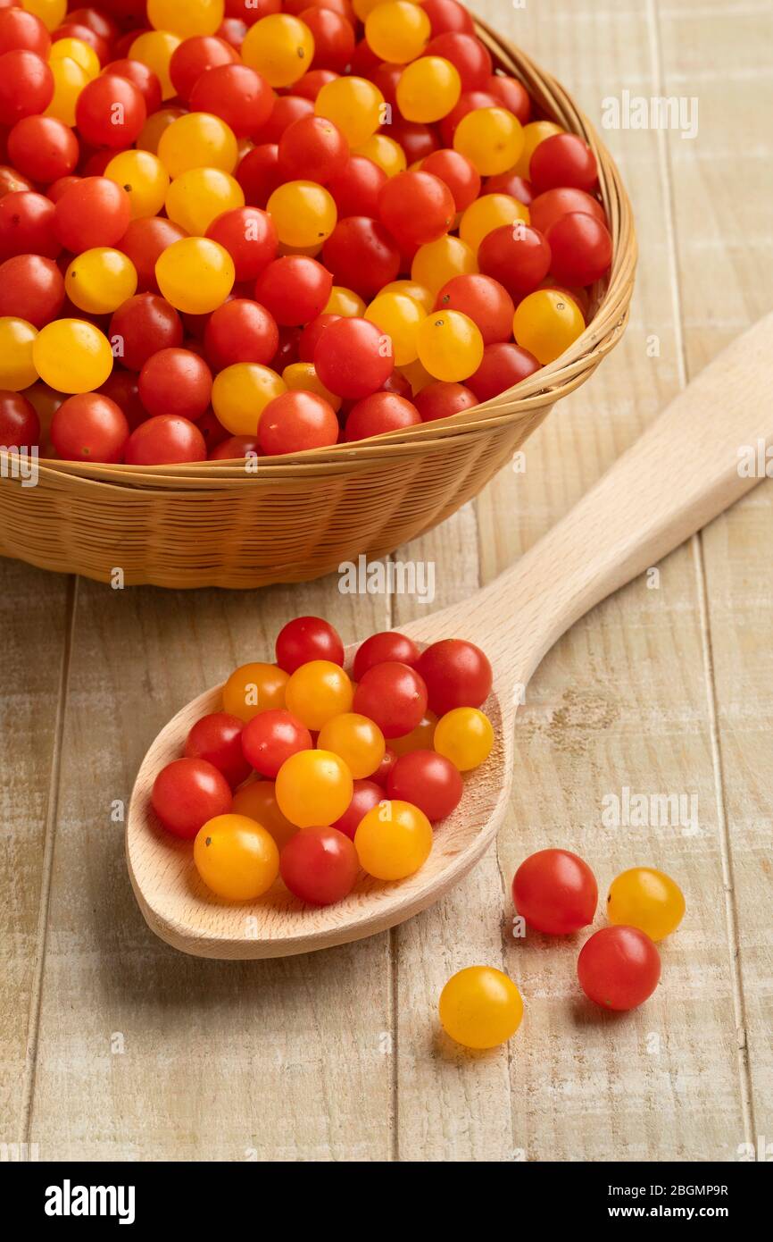 Cesto e cucchiaio di legno con pomodori freschi rossi e gialli Tomberry da vicino Foto Stock