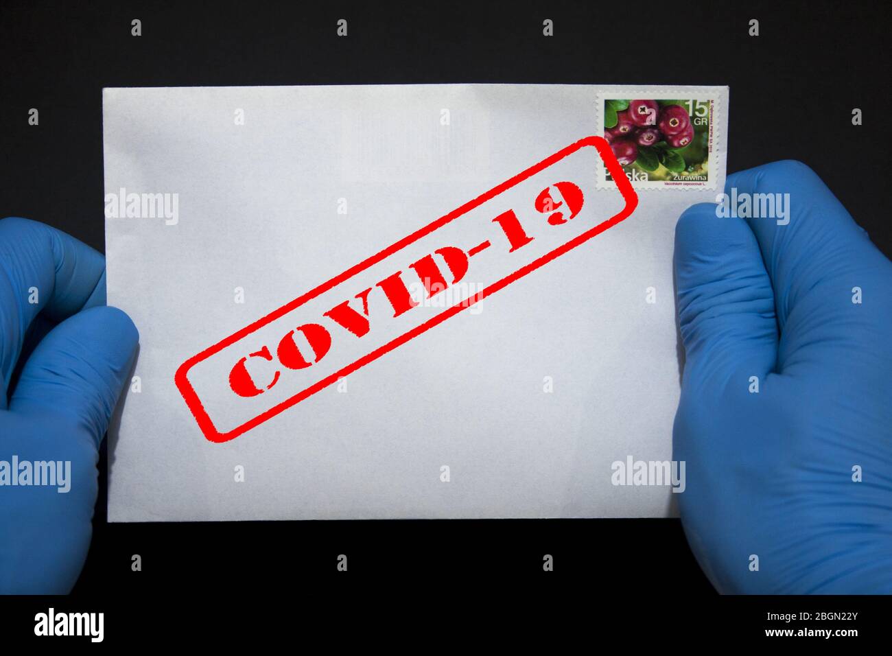 Un uomo con le mani in guanti protettivi che contiene una lettera che può contenere il virus COVID-19. Gli invii postali possono diffondere Coronavirus. Foto Stock