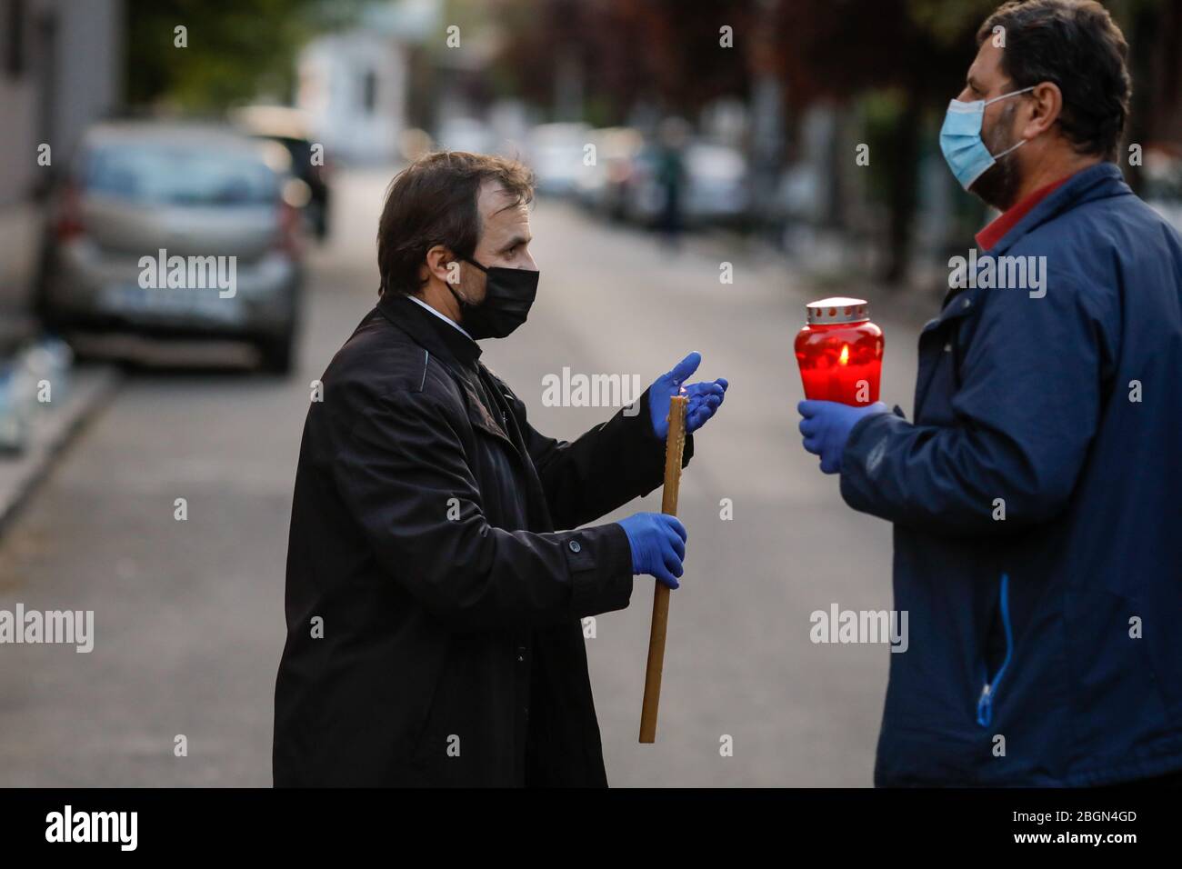Bucarest, Romania - 18 aprile 2020: Un sacerdote ortodosso che indossa guanti e maschera a causa del blocco pandemico covid-19 consegna la luce Santa durante la t Foto Stock