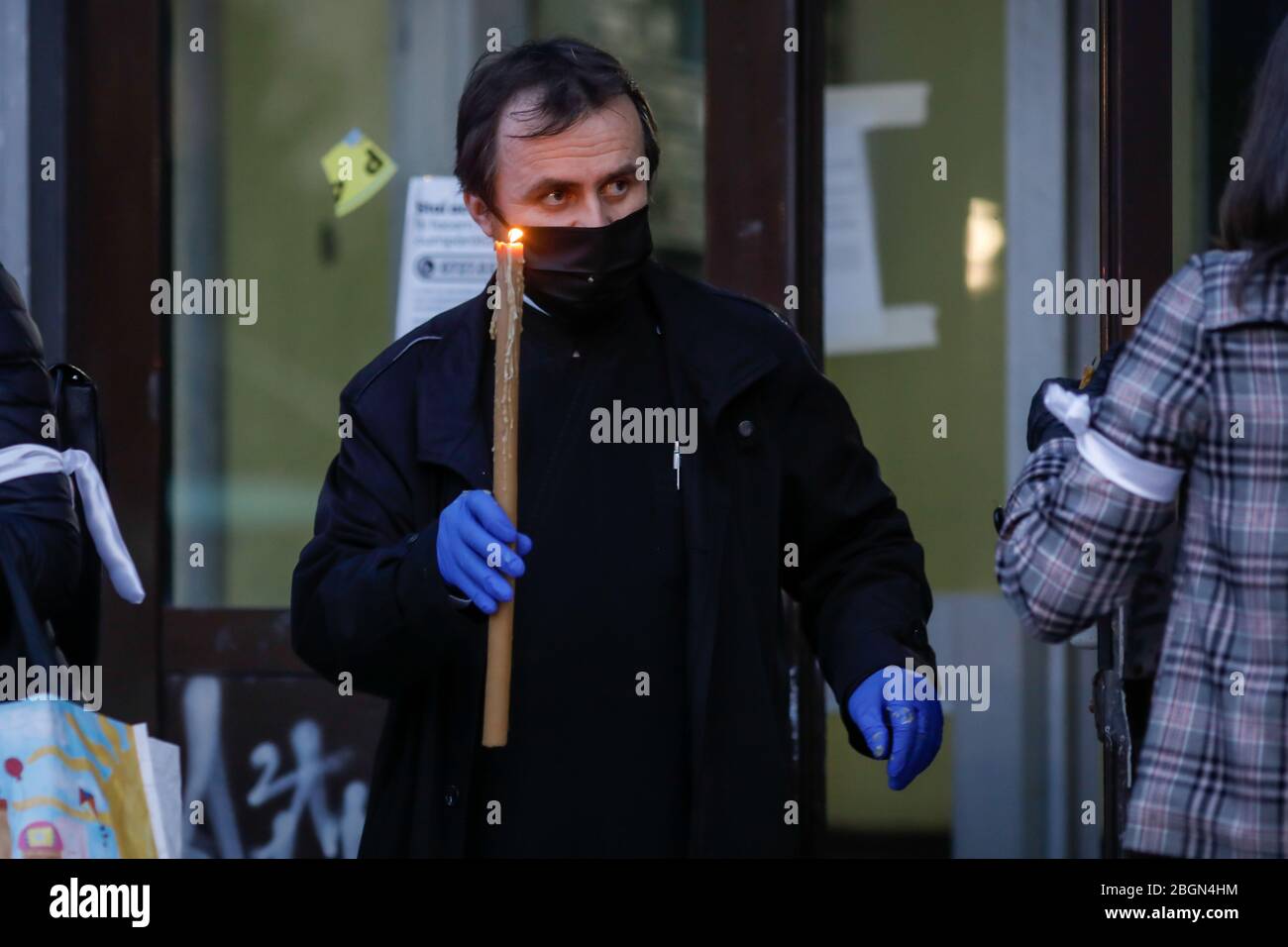 Bucarest, Romania - 18 aprile 2020: Un sacerdote ortodosso che indossa guanti e maschera a causa del blocco pandemico covid-19 consegna la luce Santa durante la t Foto Stock