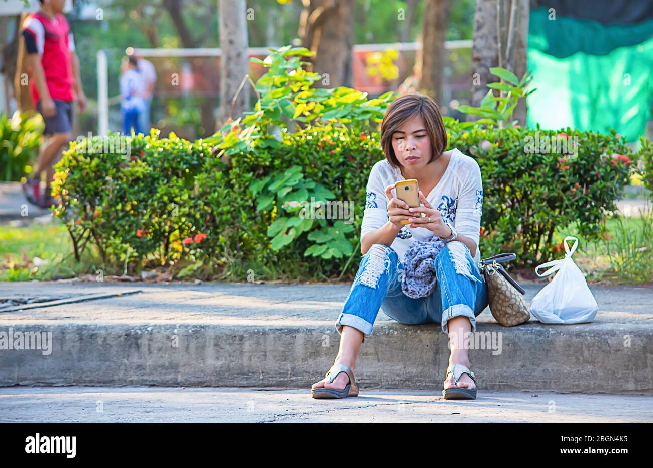 Donne asiatiche seduti sul marciapiede lungo la strada e giocare Mobile. Foto Stock