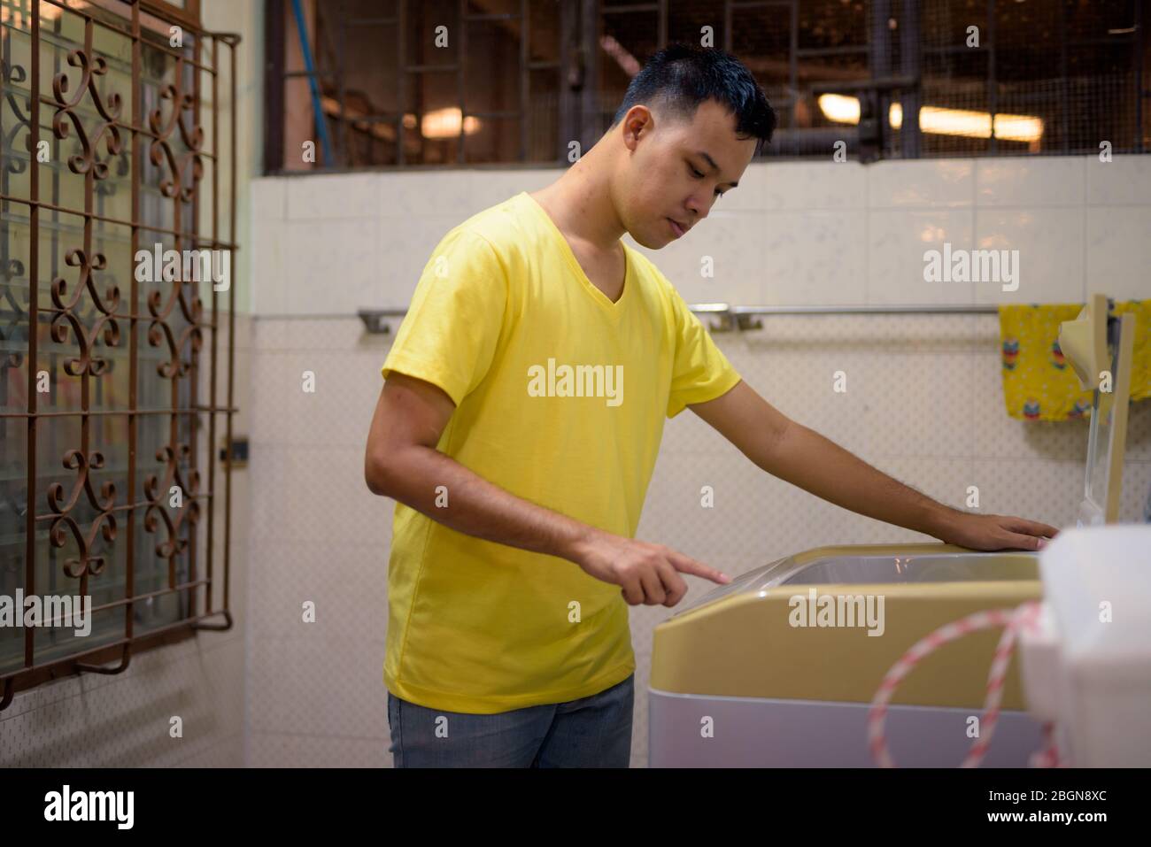 Ritratto di giovane asiatico che fa lavanderia a casa Foto Stock