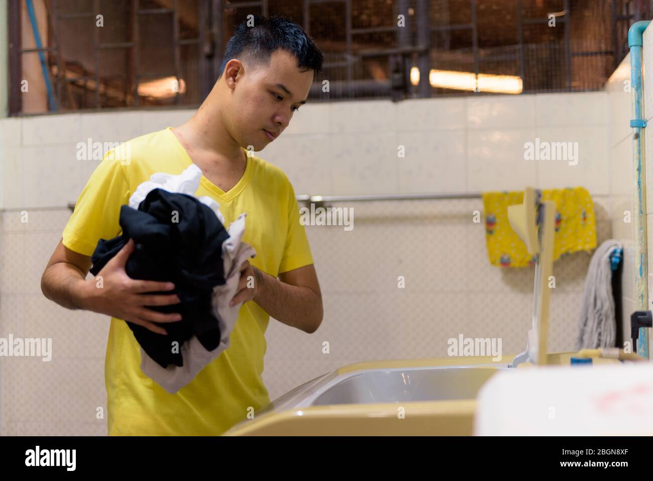 Ritratto di giovane asiatico che fa lavanderia a casa Foto Stock