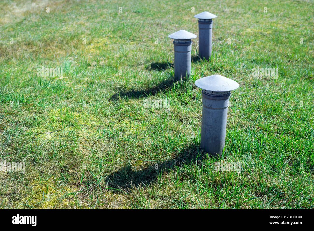 Tre tubi di ventilazione fognari che escono dal terreno nel giardino. Cappe per tubi di ventilazione nell'erba esterna Foto Stock