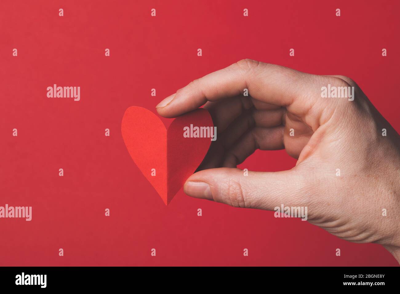 Mano femmina che tiene una carta rossa tagliato il cuore su uno sfondo rosso normale. Foto Stock