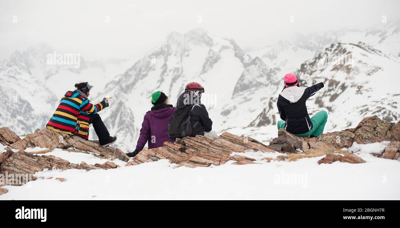 Gruppo di snowboarder e sciatori femminili e maschili, sedersi e riposare sulla roccia nella neve, e godere nel bellissimo paesaggio di rang panoramico Alpi montagna Foto Stock