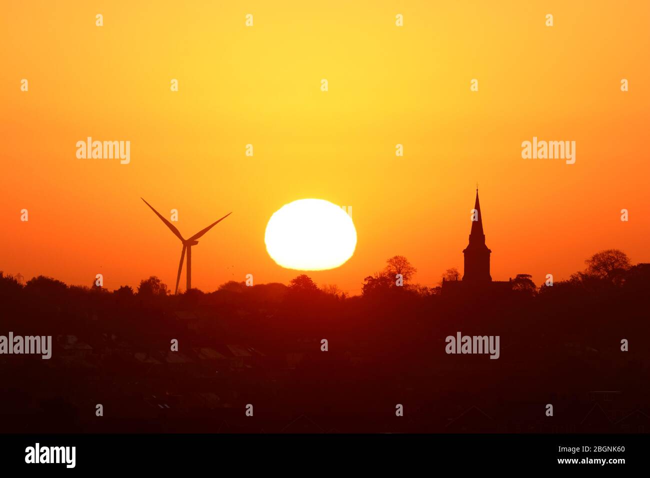 Un sole dorato che sorge dietro la chiesa di Santa Maria in Garforth & Hook Moor Wind Farm Foto Stock