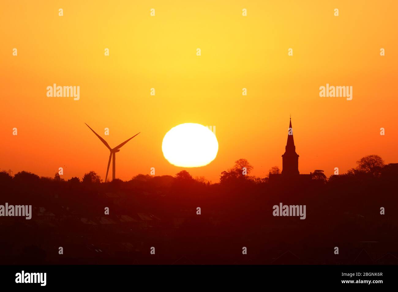 Un sole dorato che sorge dietro la chiesa di Santa Maria in Garforth & Hook Moor Wind Farm Foto Stock