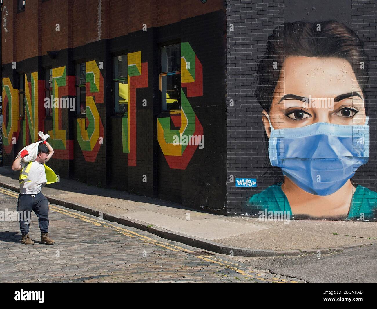 Builder che cammina oltre l'arte di strada a sostegno del NHS a Londra Est durante il blocco del virus corona. Foto Stock