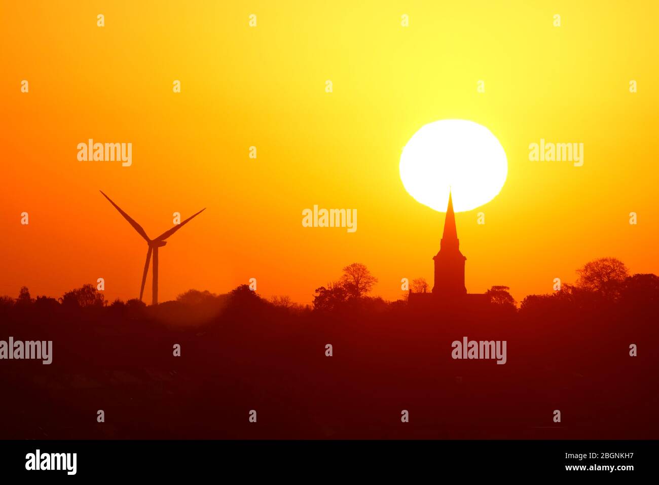 Un sole dorato che sorge dietro la chiesa di Santa Maria in Garforth & Hook Moor Wind Farm Foto Stock