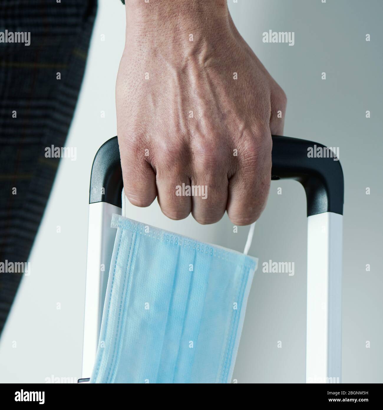 primo piano di un giovane, con una maschera chirurgica in mano, tirando una valigia per il suo manico telescopico Foto Stock