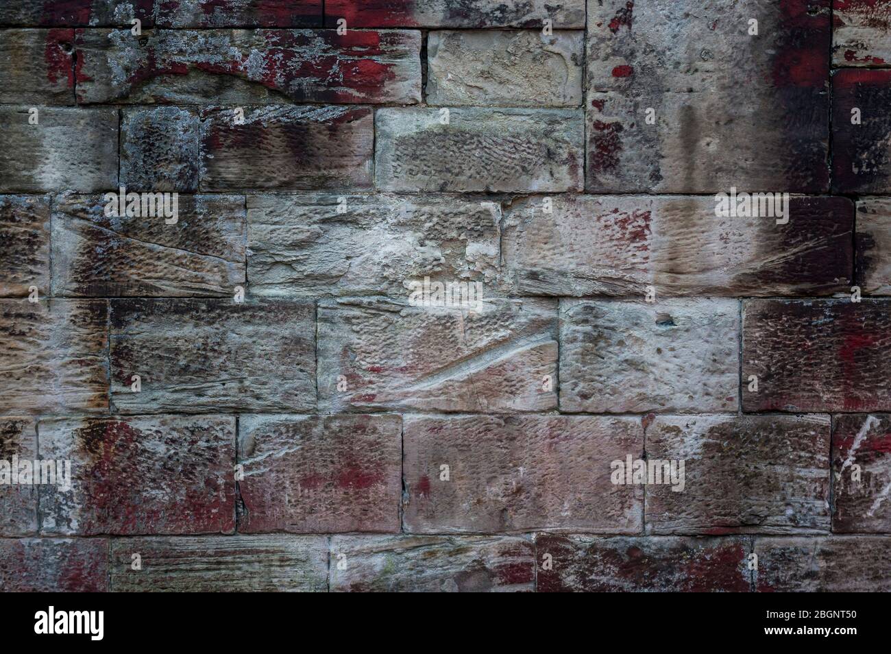 Primo piano di un vecchio muro di arenaria stagionato di pietre di diverse dimensioni e struttura con efflorescenza e macchie di colore rosso, bianco e nero Foto Stock
