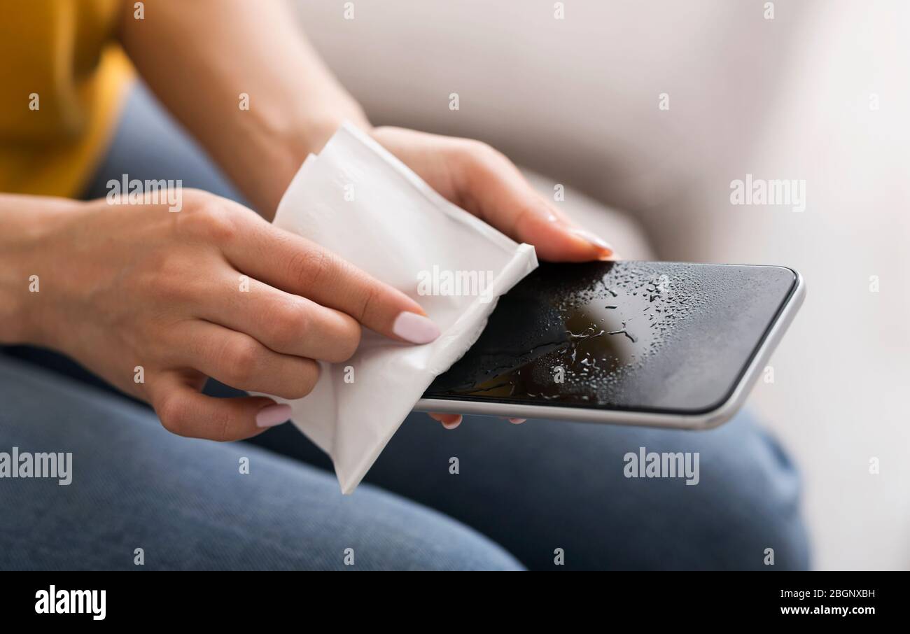 Misure igieniche COVID-19. Ragazza irriconoscibile che utilizza tovagliolo antisettico per pulire il suo smartphone in interni. Panorama Foto Stock