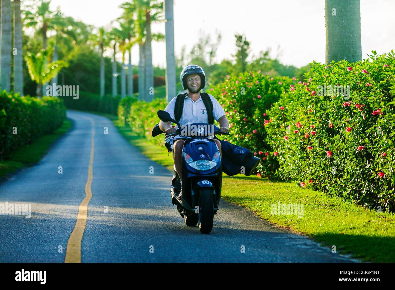 Sorridente turista maschile che trasporta golf club su scooter; Port Royal Golf Course; Bermuda Foto Stock