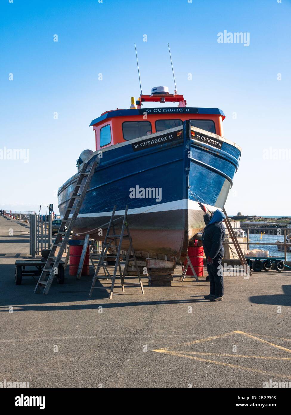 Un uomo che dipinge una barca nel porto a amble, Northumberland. Foto Stock