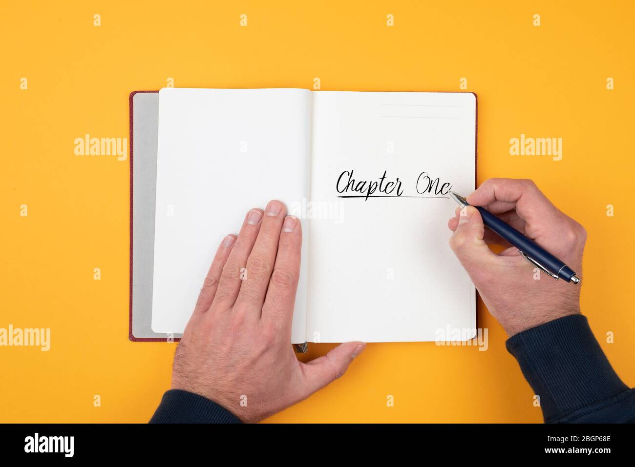 Vista superiore della persona che scrive le parole CAPITOLO UNO sul blocco note contro sfondo arancione Foto Stock