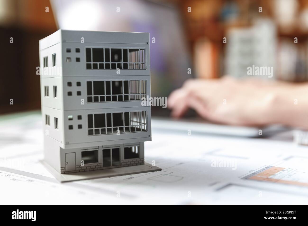 Primo piano di un modello di casa in piedi sopra piani di appartamento di fronte a un computer portatile in un ufficio di costruzione. Ufficio di architettura e costruzione c Foto Stock