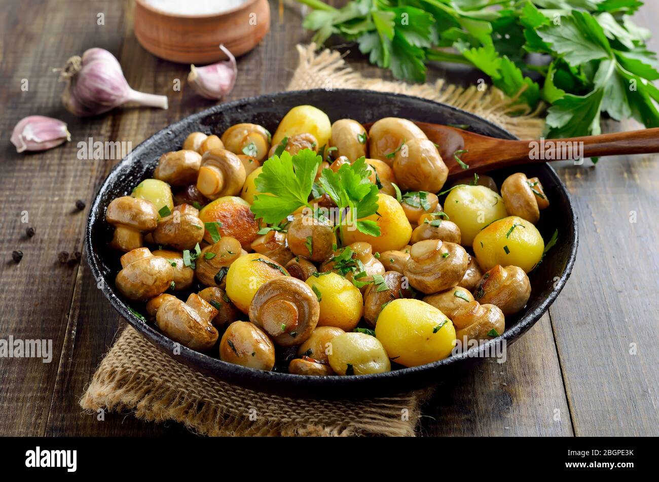 Funghi fritti con patate in teglia di ghisa su tavola di legno Foto Stock