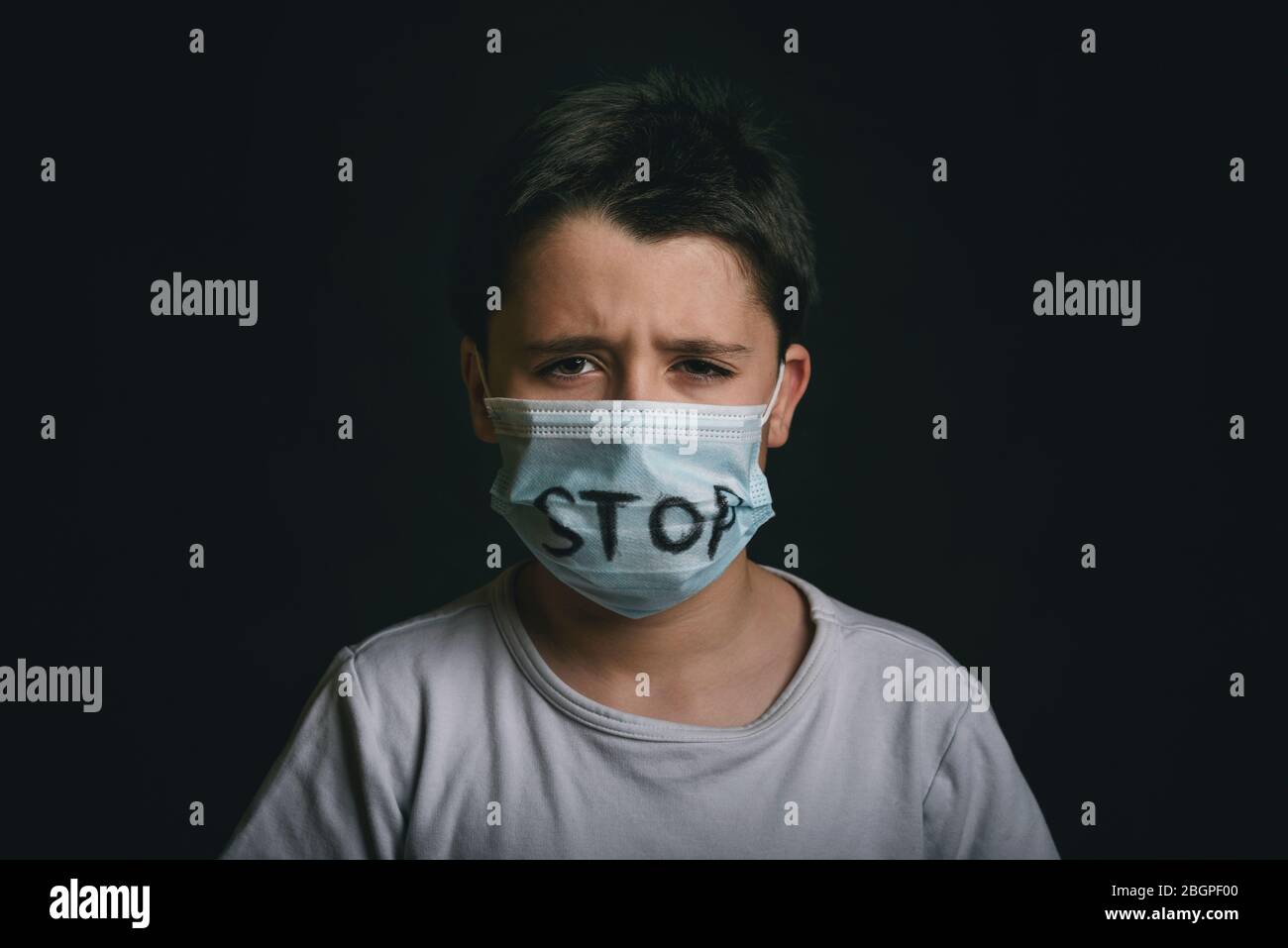 Stop, pianto bambino indossando maschera medica per il coronavirus su sfondo nero Foto Stock