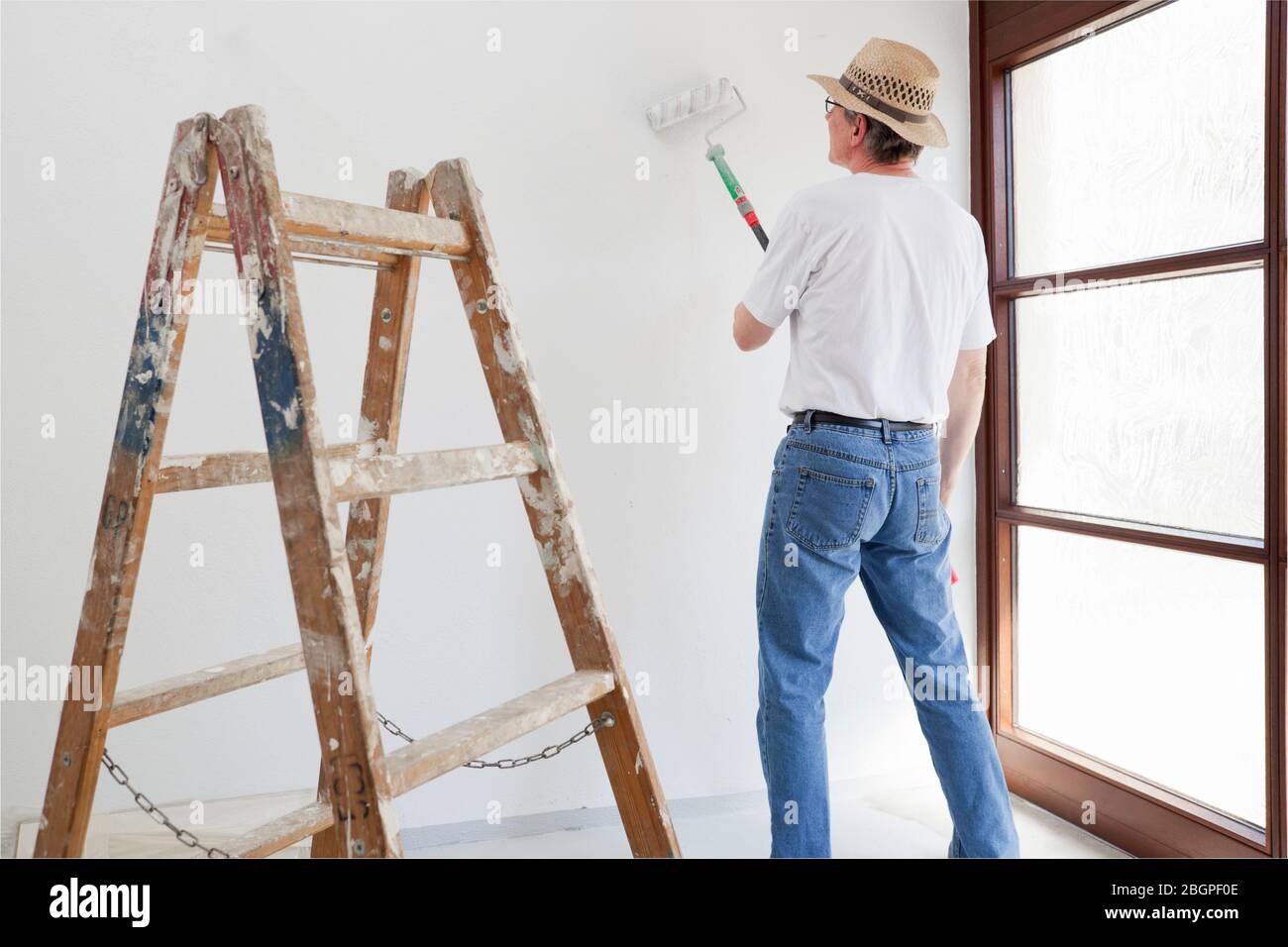 Uomo di casa o pittore professionista che dipinge una stanza nella sua casa con scala in primo piano Foto Stock