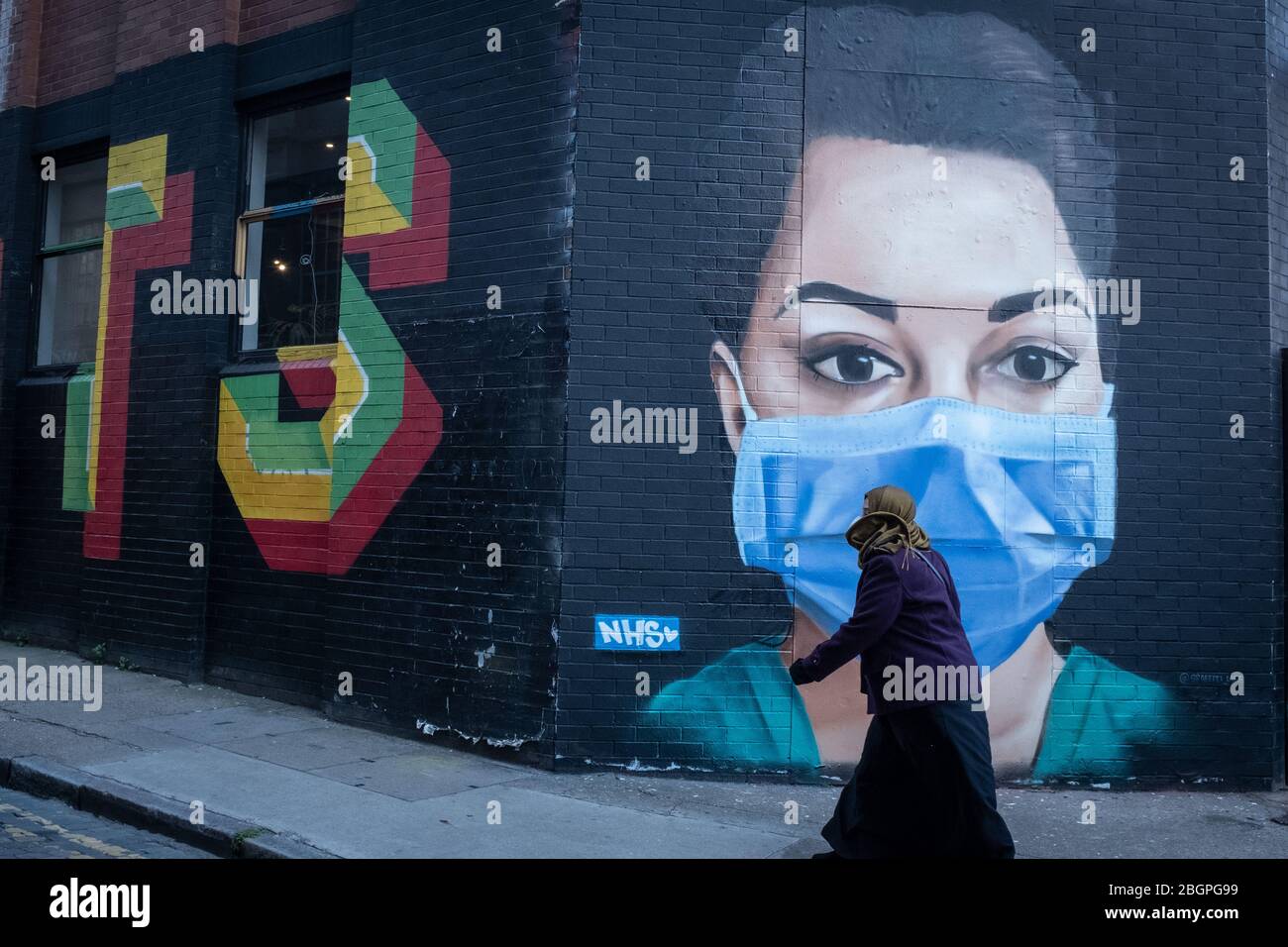 Una donna mascherata passa un murale a Shoreditch East London celebrando i lavoratori del NHS durante la pandemia del coronavirus. Foto Stock