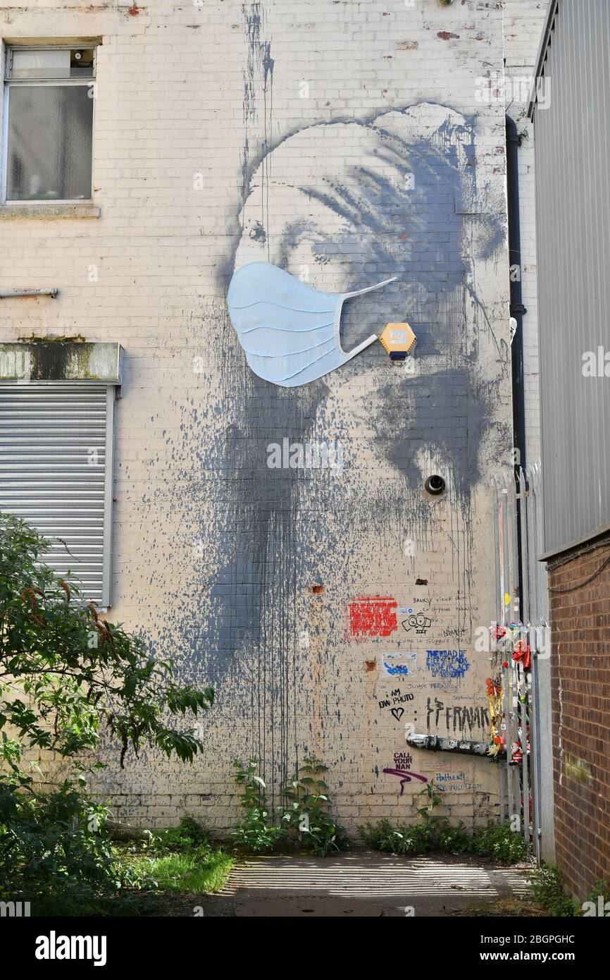 Banksy's Girl con un murale di timpano trafitto è stata data una maschera facciale in un cenno alla pandemia di coronavirus, a Hanover Place a Bristol, come il Regno Unito continua in blocco per contribuire a frenare la diffusione del coronavirus. Foto Stock