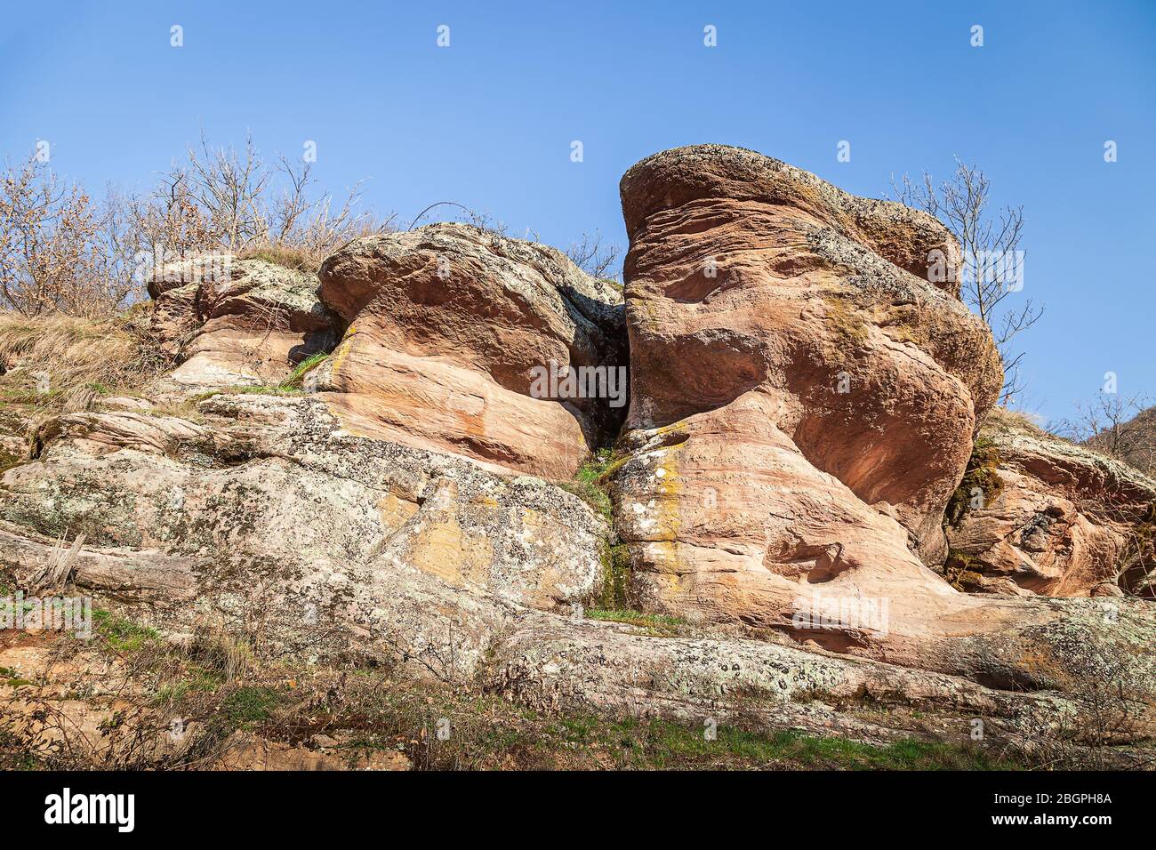 Belle forme di rocce rosse erose coperte da muschio dorato e illuminato dal sole sotto un cielo blu in un canyon in Serbia chiamato Small Colorado Foto Stock