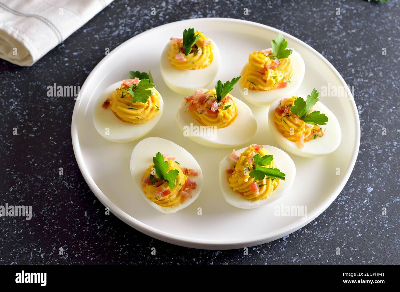 Uova farcite con tuorlo d'uovo, pancetta, senape e prezzemolo su piatto bianco Foto Stock