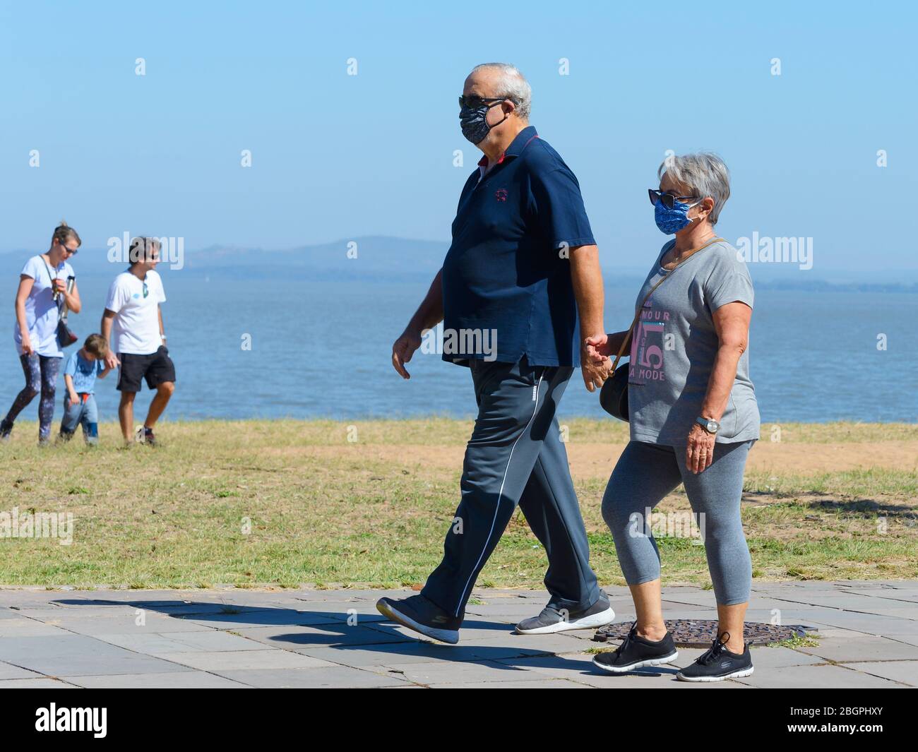 Vecchia coppia che cammina all'aperto usando maschere facciali durante il periodo di quarantena di Coronavirus. Fuori fuoco giovane famiglia non usando maschera durante COVID 19 focolaio. Foto Stock
