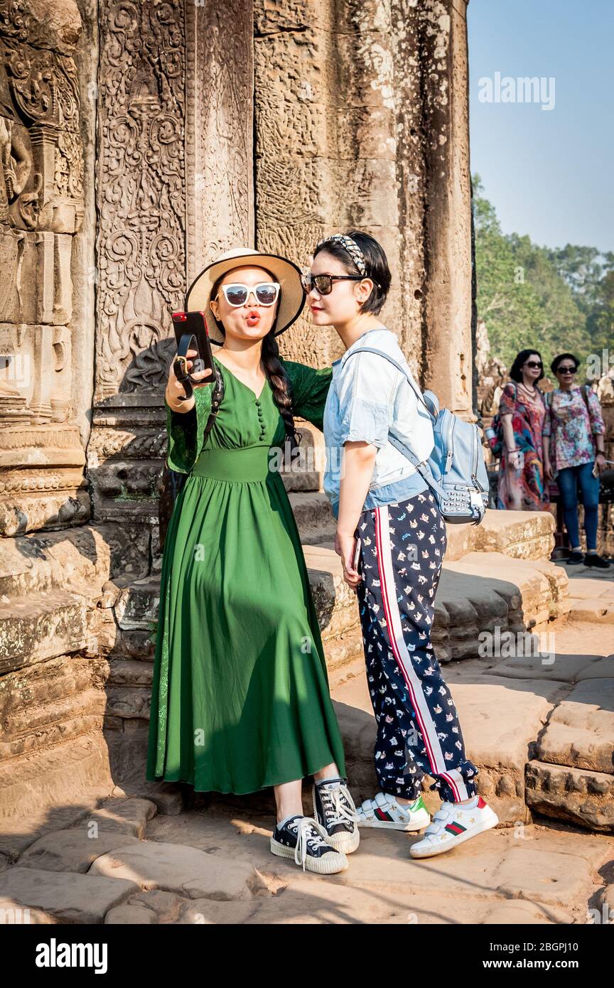 I turisti asiatici fanno il loro senso attraverso i templi antichi di Angkor Wat, Cambogia. Prendendo selfie, scalando scale, camminando i corridoi e prendendo Foto Stock