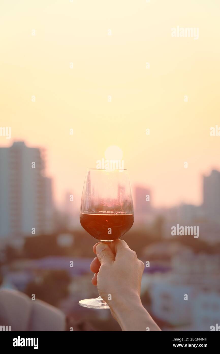 Mano della donna che tiene i bicchieri di vino rosso sul balcone durante il tramonto, concetto di festa Foto Stock