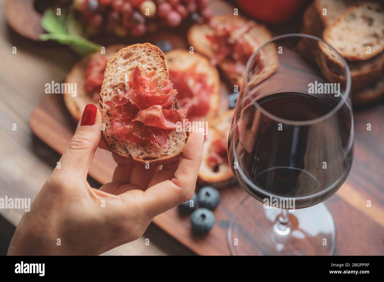 Foucs selettivo su finger holding prosciutto jamon serrano e bicchieri di vino rosso su tavola di legno Foto Stock