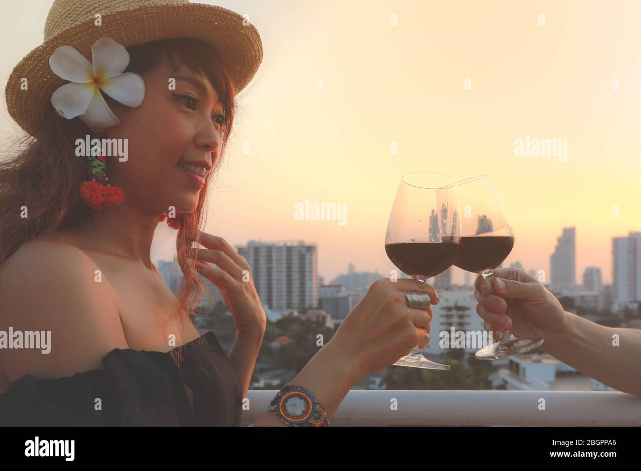Bella giovane donna asiatica tostando il bicchiere di vino rosso sulla terrazza, stile vintage Foto Stock