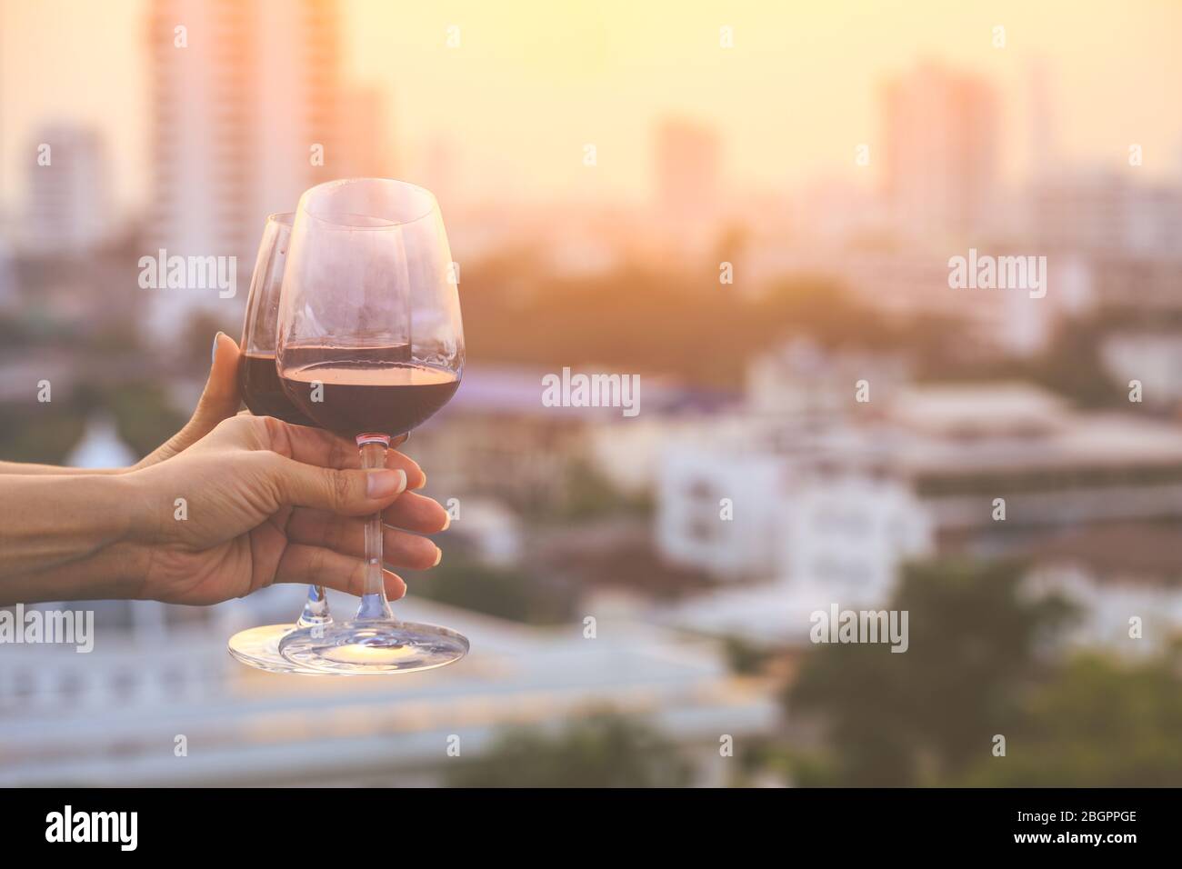 primo piano sulle mani tenendo bicchieri di vino rosso sul balcone durante il tramonto, concetto di celebrazione Foto Stock