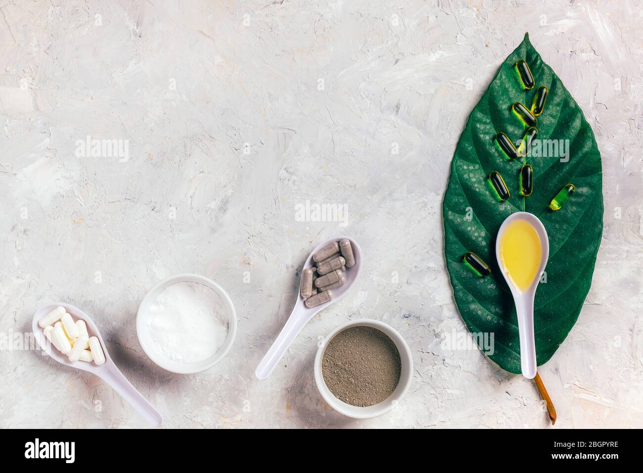 Capsule olio di pesce omega-3, pillole bianche e grigie, polvere e olio in cucchiai sulla foglia verde e bianco sfondo rustico. Concetto di salute e bellezza. Foto Stock
