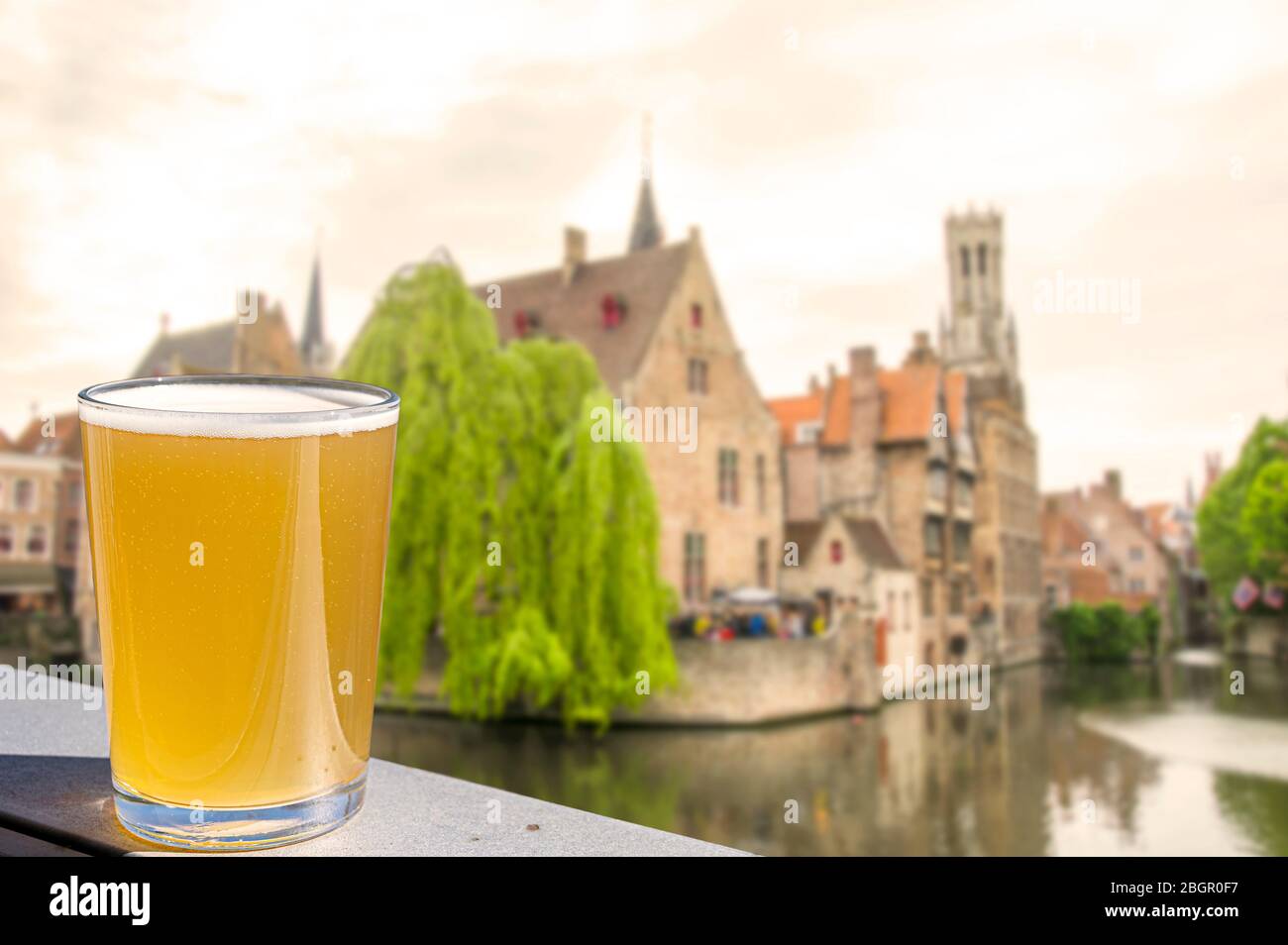 Bicchiere di birra con vista sulle case storiche, sul canale e sulla torre campanaria nel centro di Bruges, Belgio. Foto Stock