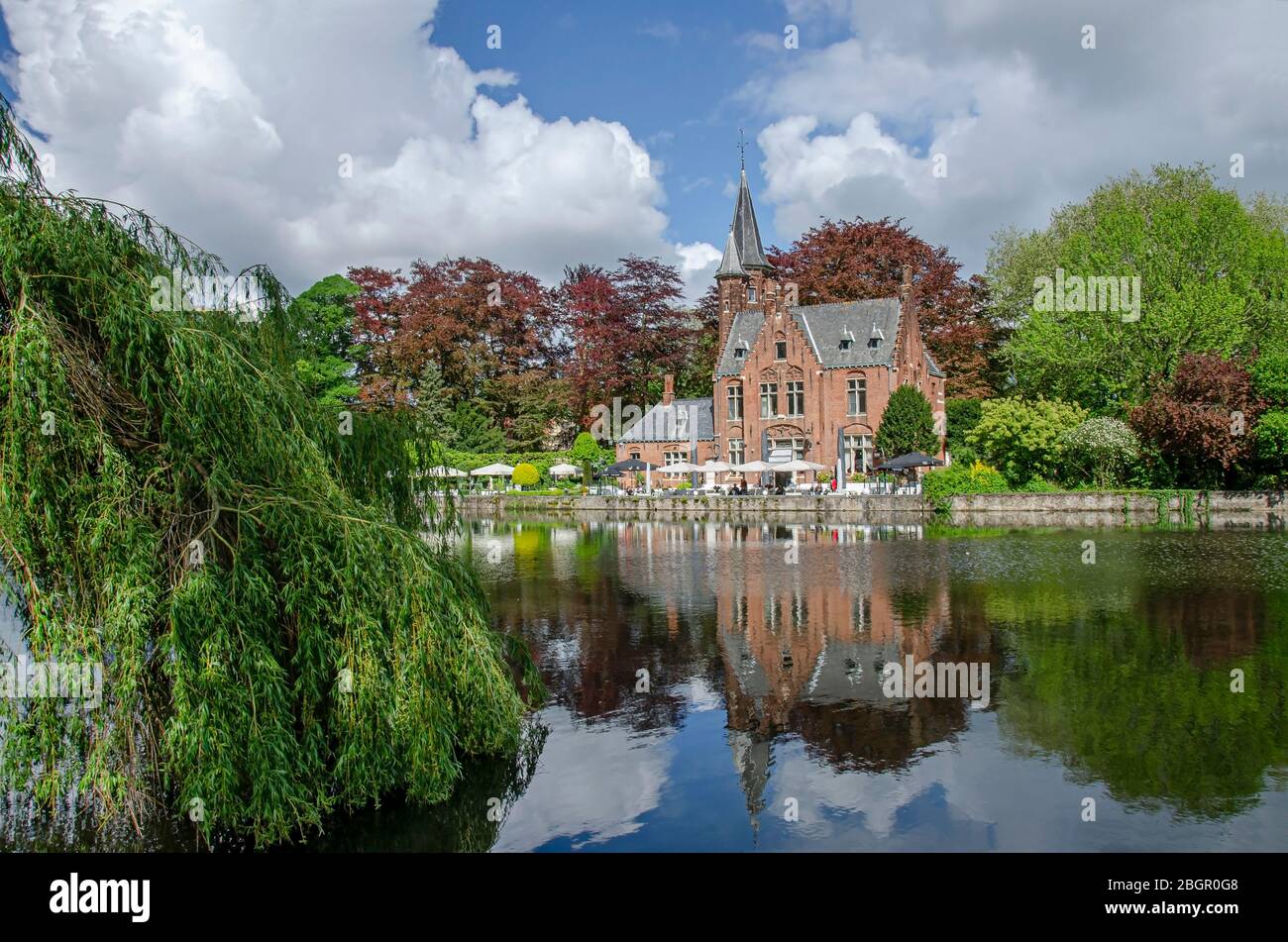 Vista sul tranquillo spazio verde pubblico con il lago Minnewater e il piccolo castello di Bruges durante la giornata di sole in primavera, in Belgio Foto Stock