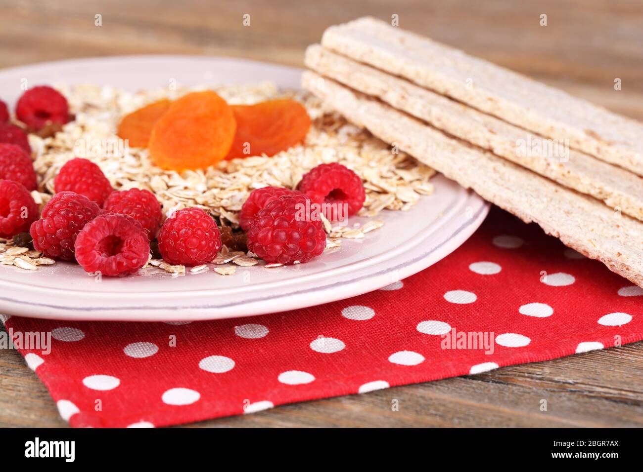 Piatto grande con farinata d'avena, pani di pane e frutti di bosco su un tovagliolo con palline di polka su sfondo di legno Foto Stock