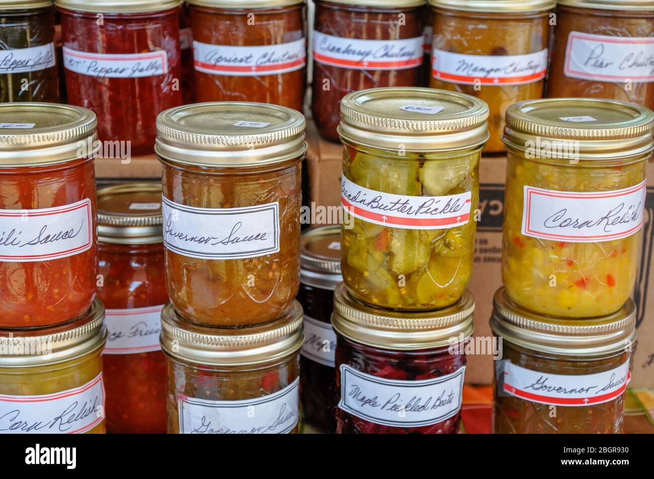 Vasi colorati accatastati di marmellate fatte in casa, gelatine, chutneys e altre conserve riempire un tavolo presso un mercato contadino locale. Foto Stock