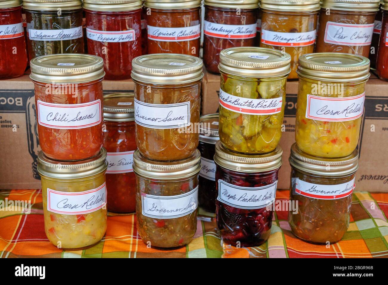 Vasi colorati accatastati di marmellate fatte in casa, gelatine, chutneys e altre conserve riempire un tavolo presso un mercato contadino locale. Foto Stock