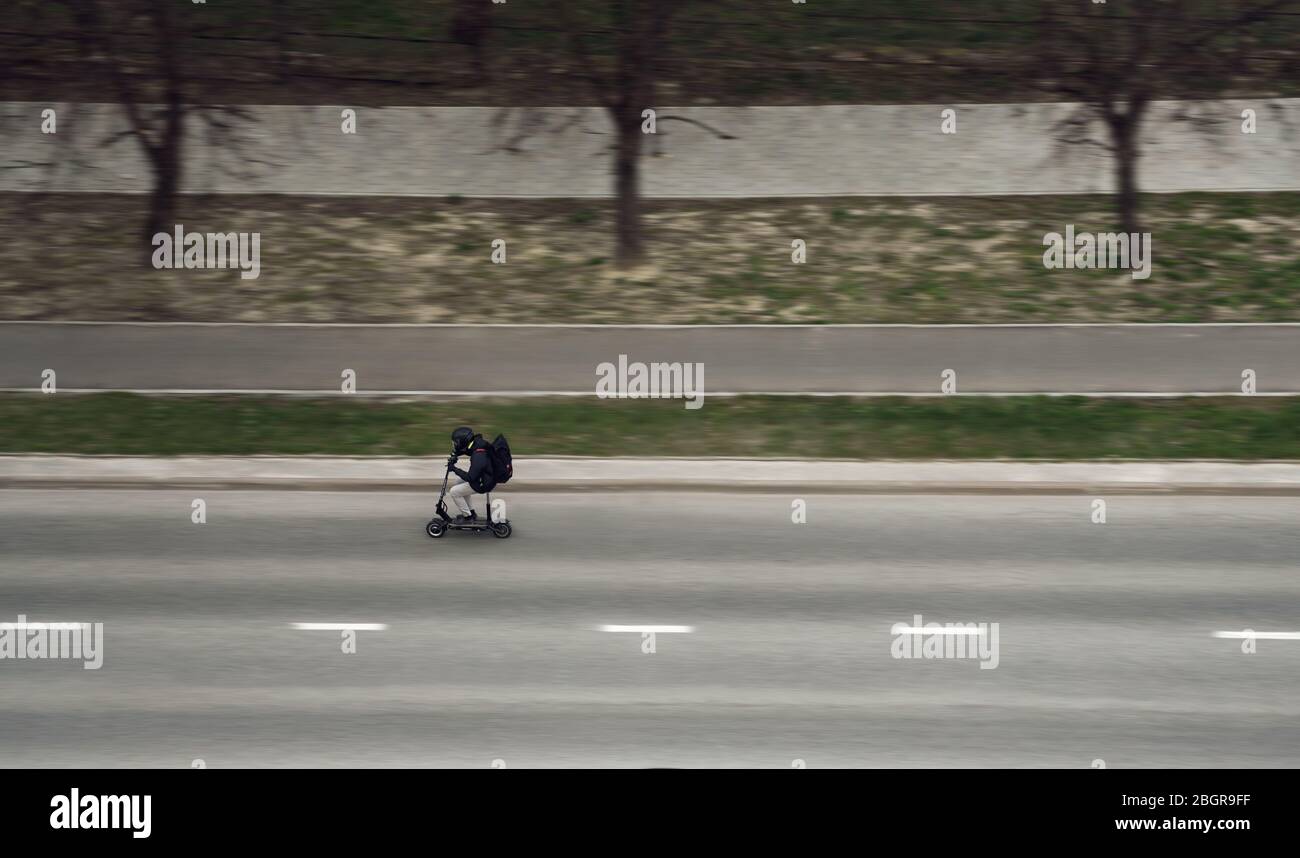 Vista laterale di un uomo che indossa il casco su scooter elettrico in strada Foto Stock