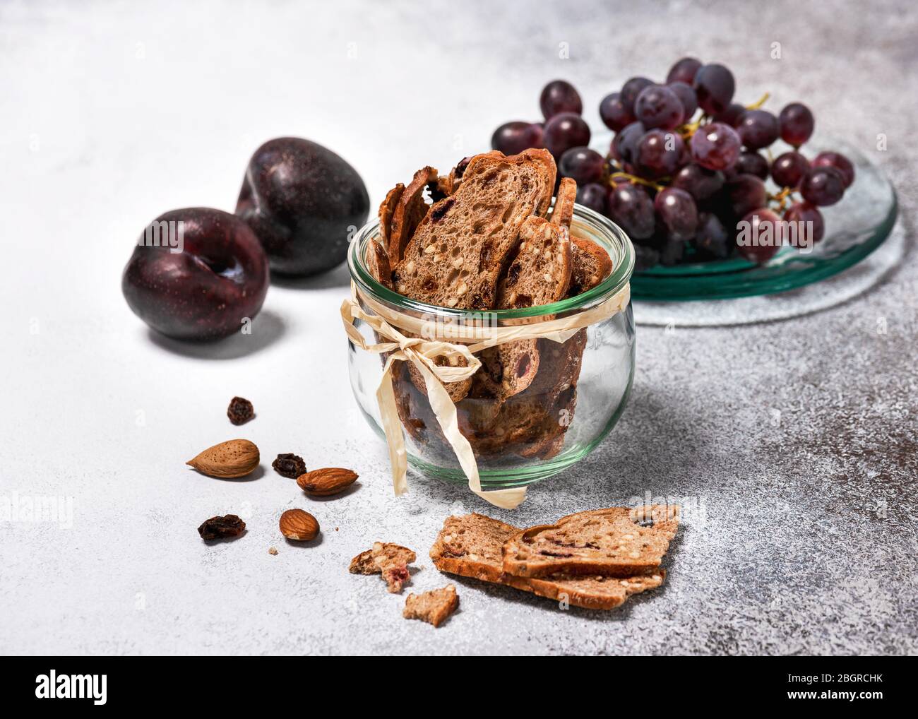 Fette di pane secco alla frutta in un vaso di vetro con prugne e uva fresche. Concetto di cibo sano fatto in casa. Messa a fuoco selettiva. Foto Stock