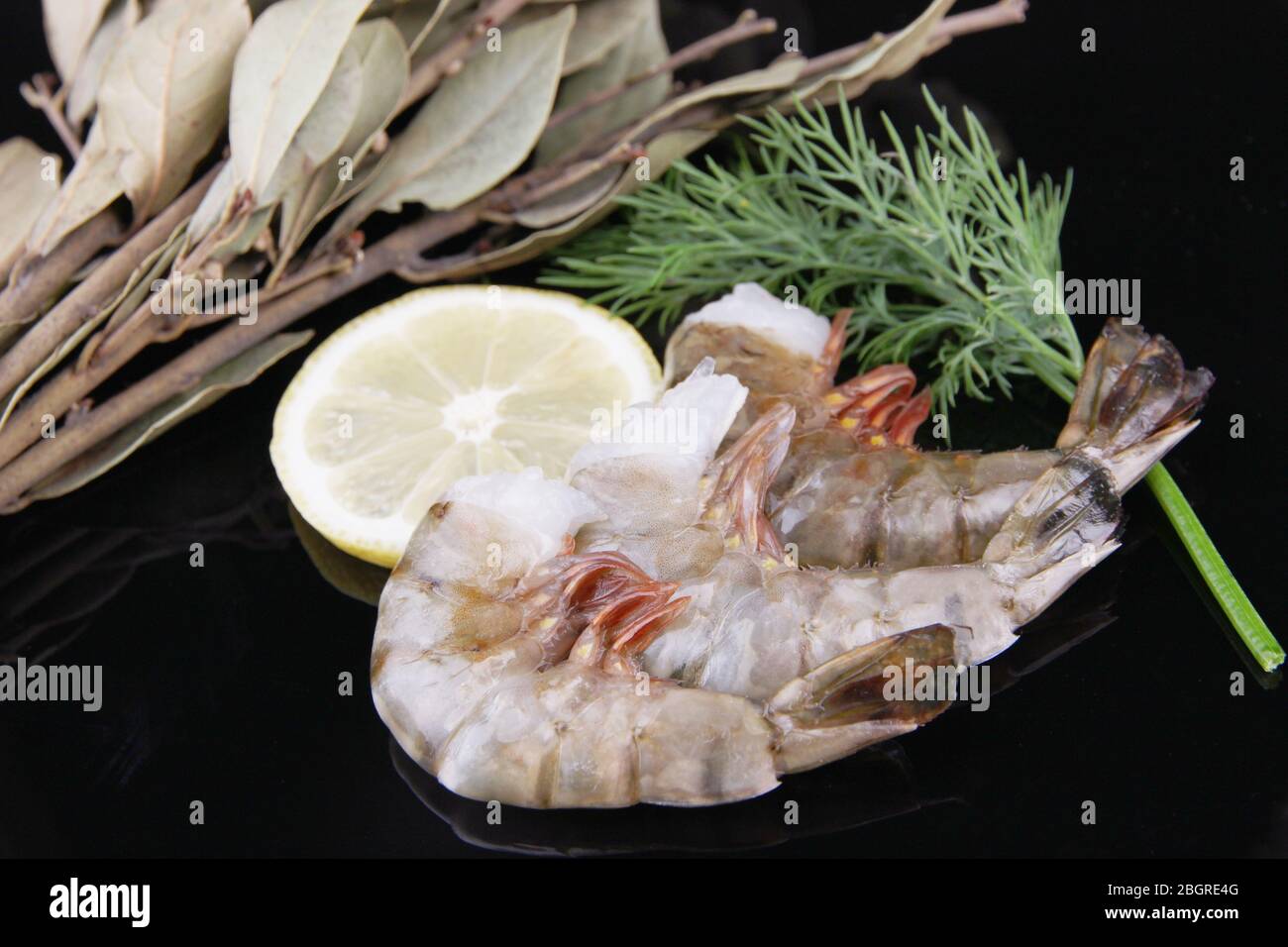 Gamberi freschi e gustosi con limone, foglie di alloro e aneto su sfondo nero Foto Stock