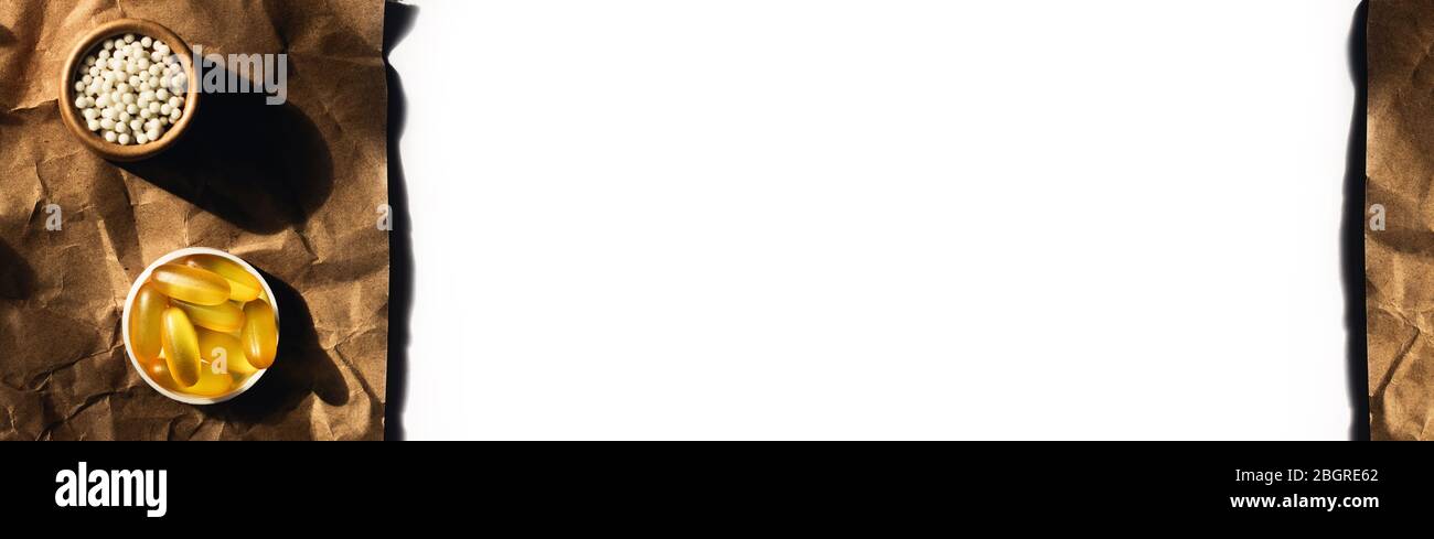 Vista dall'alto sulle capsule di olio di pesce e le palle omeopatiche giacciono su carta da imballaggio stropicciata. Circondato da rametti di eucalipto e lavanda. Foto Stock