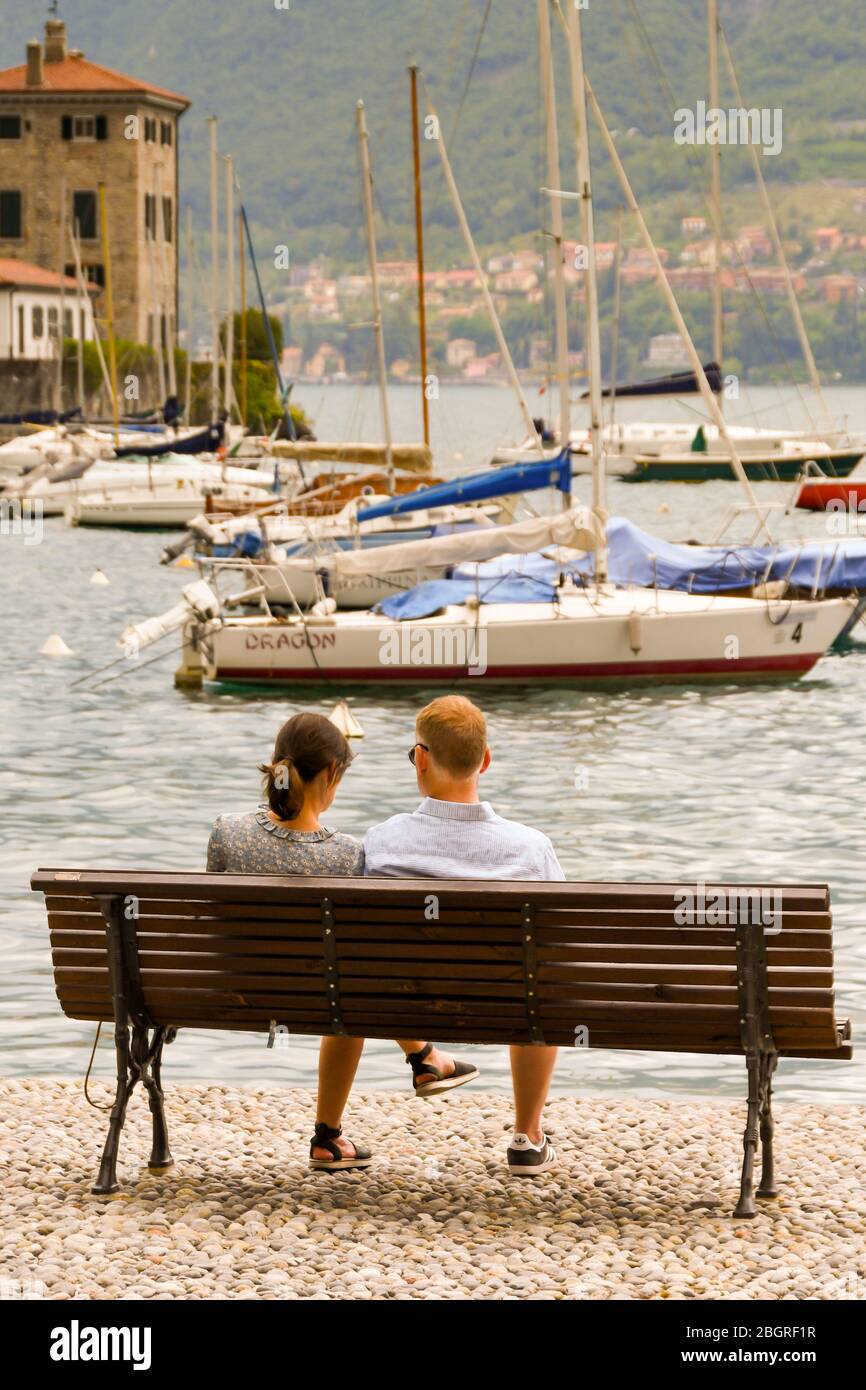 BELLAGIO, LAGO DI COMO, ITALIA - GIUGNO 2019: Uomo e donna seduti su una panca in legno che si affaccia sul porto di Bellagio sul Lago di Como. Foto Stock