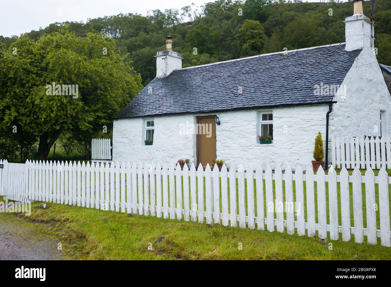 Caratteristico cottage tradizionale imbiancato a calce con recinto di palaminazione bianca e tetto piastrellato in Appin, Argyll e Bute, Scozia Foto Stock